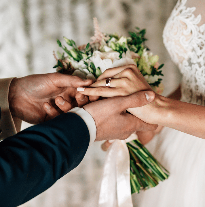 Groom placing a ring on bride’s finger while she holds a bouquet